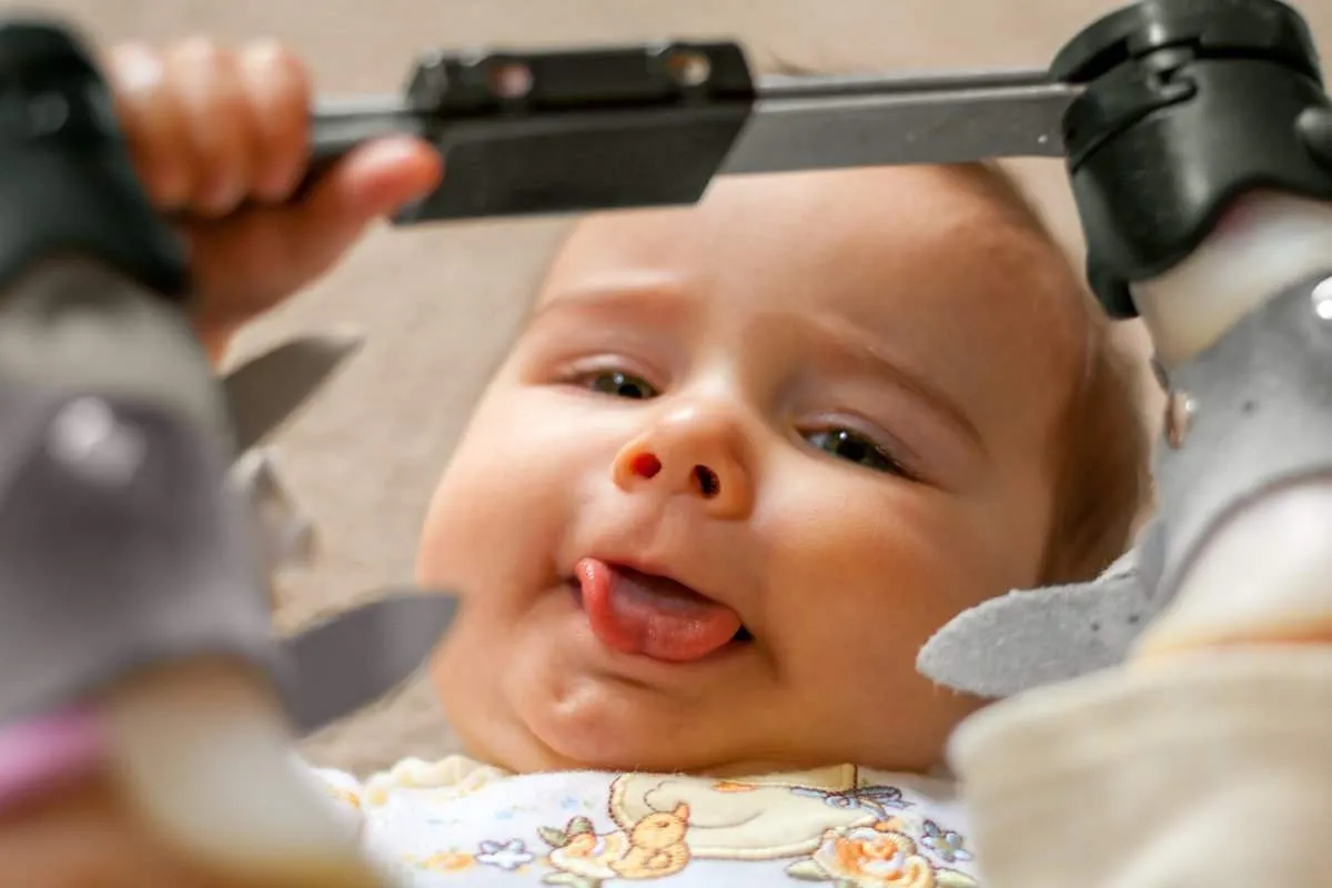 Happy Baby with Tongue Tie and Orthopedic Shoes A nine month old baby with a tongue tie and orthopedic shoes lays on her back with her tongue sticking out as much as possible as she holds the bar between her orthopedic shoes that she wore for a club foot.