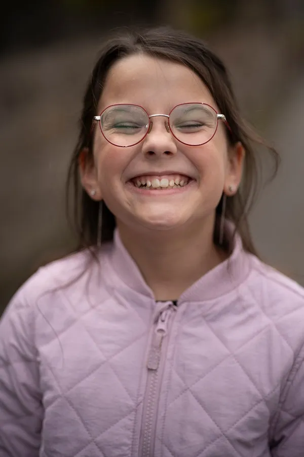 Smiling girl in glasses and a pink jacket showing her teeth outdoors, soft natural light, blurred background, copy space. Concept of dental health, confidence, and childhood joy. Smiling girl in glasses and a pink jacket showing her teeth outdoors, soft natural light, blurred background, copy space. Concept of dental health, confidence, and childhood joy.
