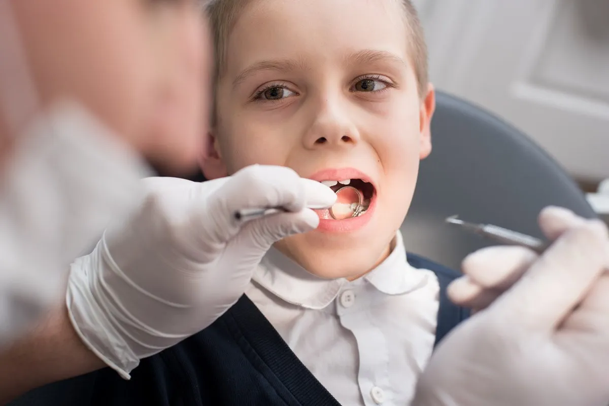 Close-up dentist examining teeth of boy patient in dental clinic using dental tools - probe and mirror. Dentistry