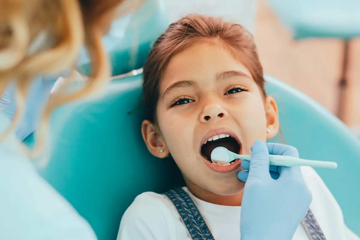 Mixed race girl getting her teeth examined with dental mirror