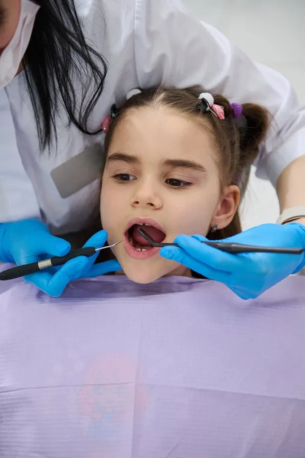 Close-up of little child girl in dentist's chair, being examined by a doctor dentist, curing caries in dentistry clinic Close-up portrait little child girl in dentist chair, being examined by a doctor dentist. Dental hygienist holding dental tools, performing teeth treatment, curing caries in pediatric dentistry clinic