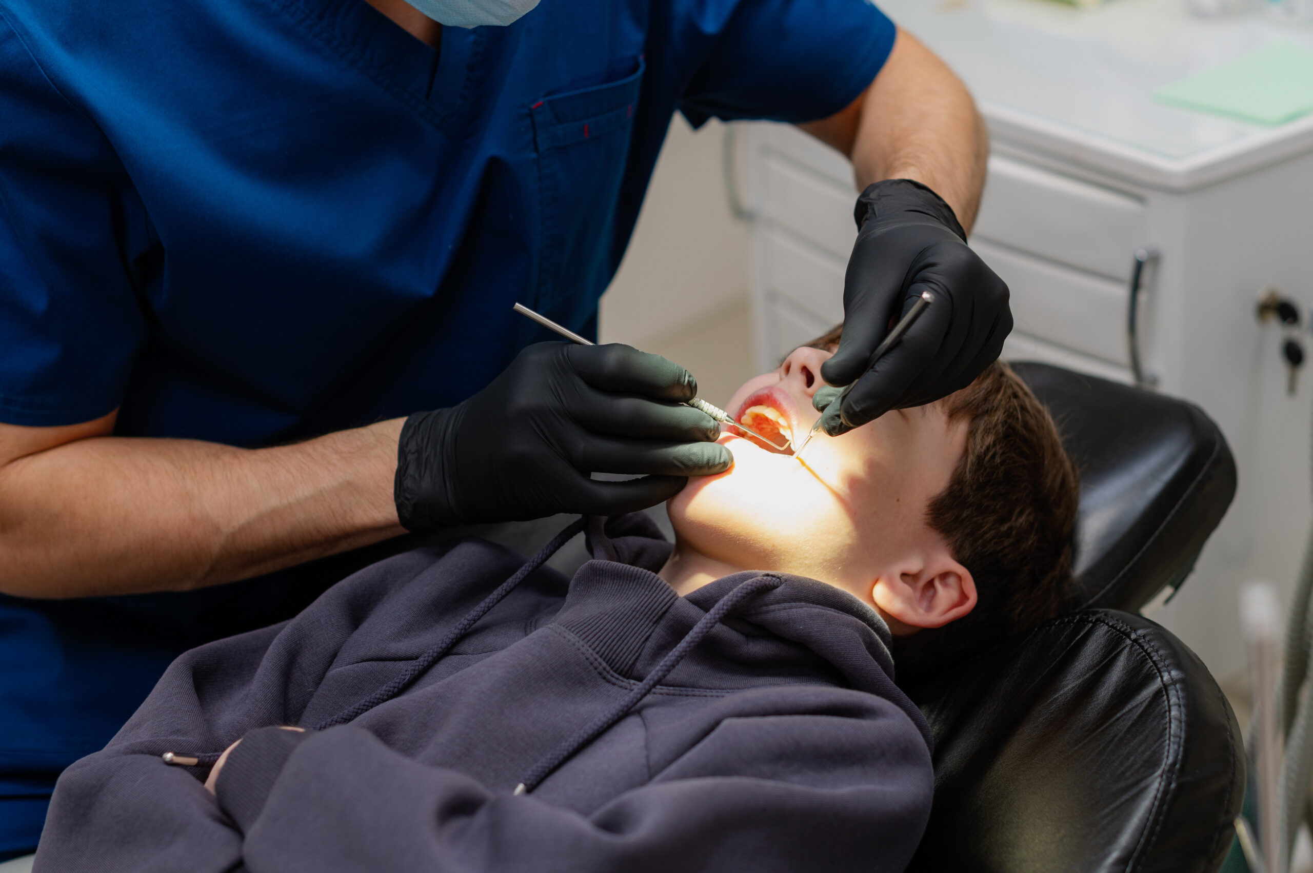 A dentist checks the teeth of a child who is sitting in an armchair with his mouth wide open. Routine dental check-up. Health A dentist checks the teeth of a child who is sitting in an armchair with his mouth wide open. Routine dental check-up. Health