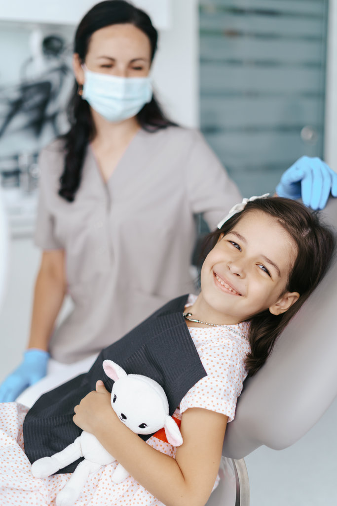Cute little girl sitting on a modern dental chair and having dental consultation with dentist