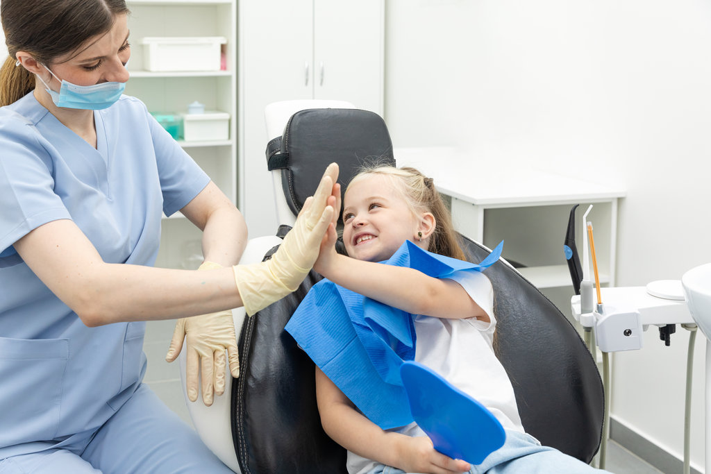 Little patient girl sitting in a chair gives a high five to a pediatric dentist after dental treatment at a clinic with modern equipment. Concept of modern and painless treatment of children's teeth. Little patient girl sitting in a chair gives a high five to a pediatric dentist after dental treatment at a clinic with modern equipment. Concept of modern and painless treatment of children's teeth.