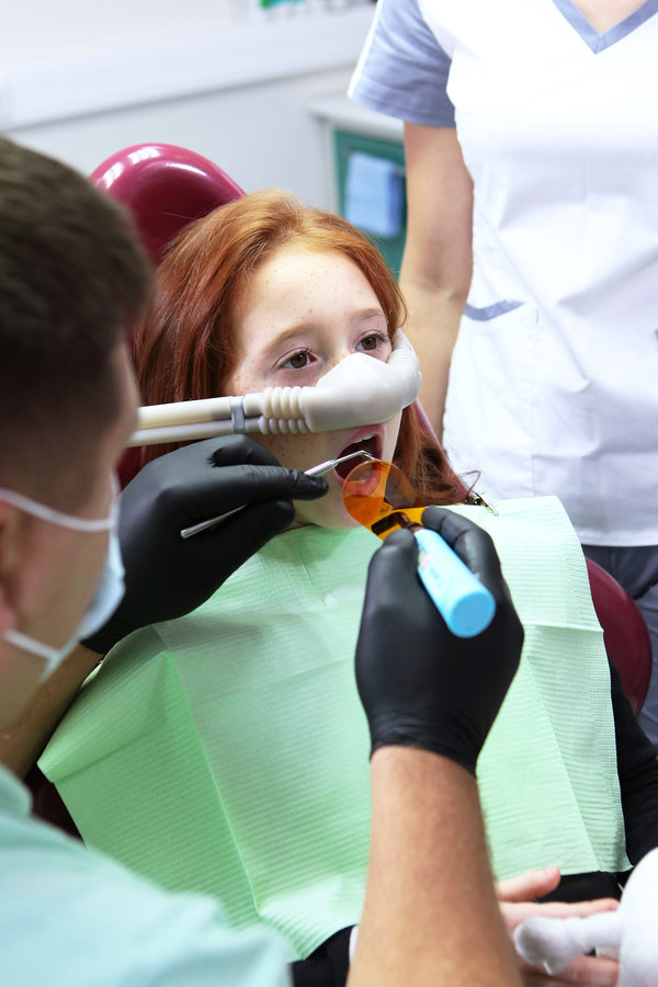 Dental treatment in a child with sedation. A little girl is injected with an inhalation sedative during dental treatment at a dental clinic. Vertical photo. Dental treatment in child with sedation. Little girl is injected with an inhalation sedative during dental treatment at dental clinic. Vertical photo.