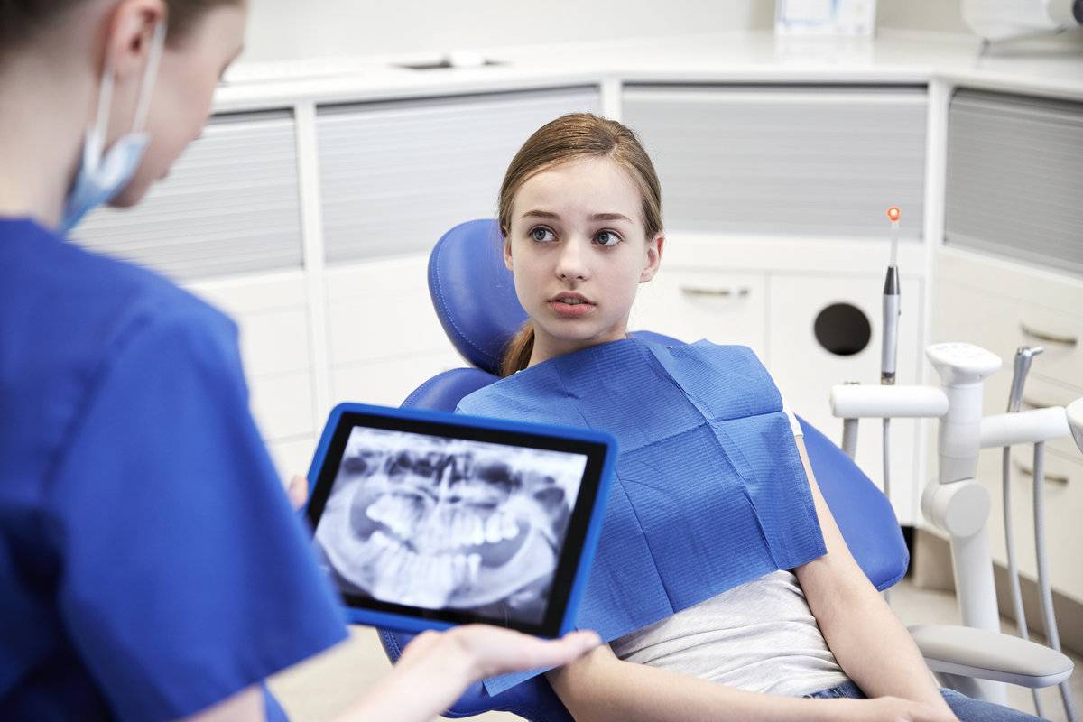 people, medicine, stomatology, technology and health care concept - female dentist showing teeth x-ray on tablet pc computer to patient girl at dental clinic office