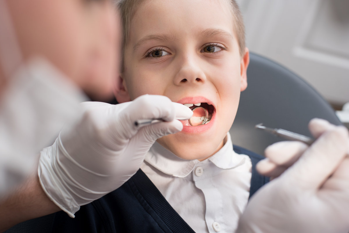 Close-up dentist examining teeth of boy patient in dental clinic using dental tools - probe and mirror. Dentistry