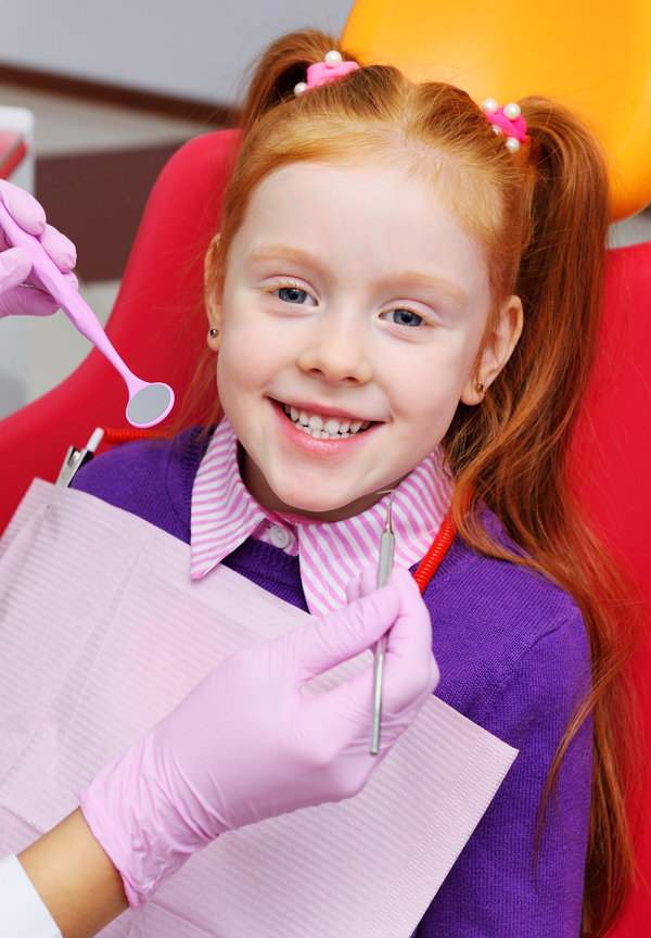 children's dentist examines the teeth and mouth of the child - a cute red-haired girl sitting in a dental chair. children's dentist examines the teeth and mouth of the child - a cute red-haired girl sitting in a dental chair. Pediatric dentistry