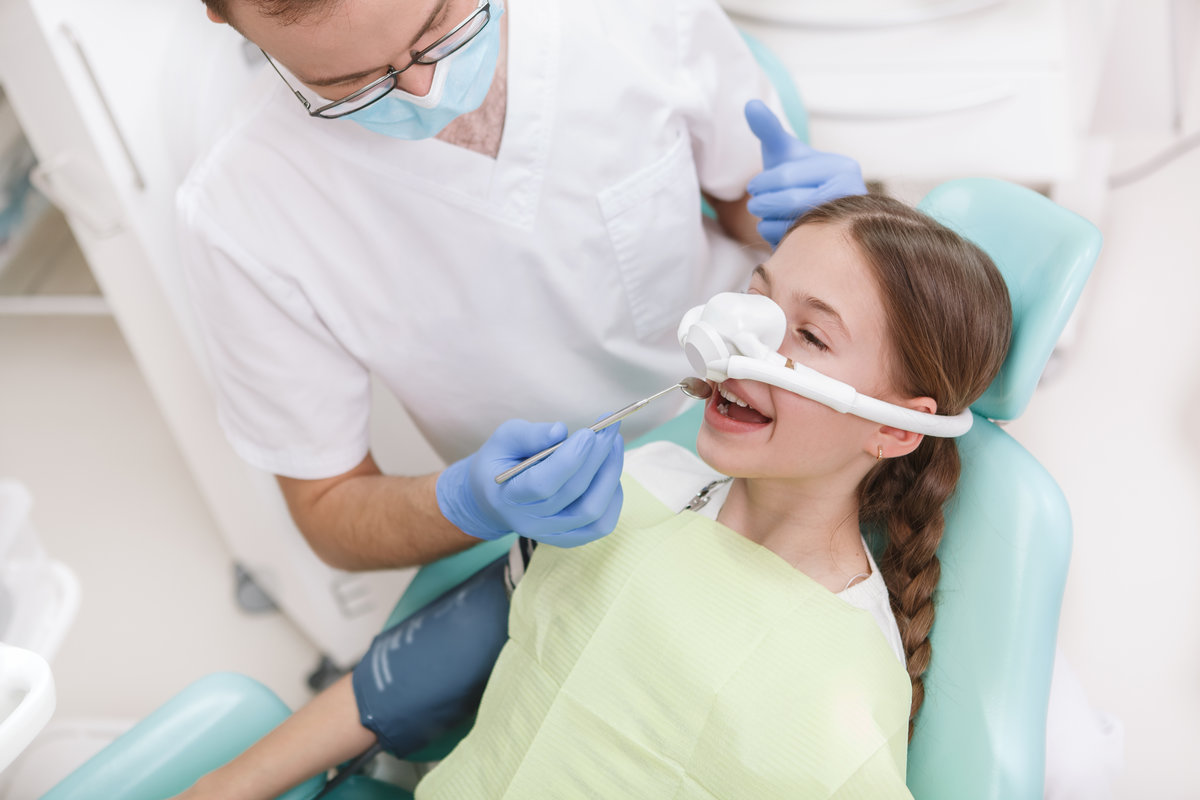 Young girl having her teeth treated while having inhalation sedation mask on