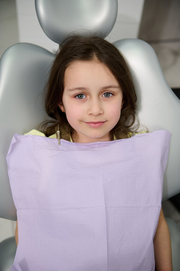 Child girl in dentist chair, ready to get a dental treatment or prophylactic checkup of baby teeth in dentistry clinic Top view. Beautiful Caucasian child, lovely little girl in dentist's chair, smiling looking at camera, ready to get a dental treatment or regular prophylactic checkup of baby teeth in dentistry clinic