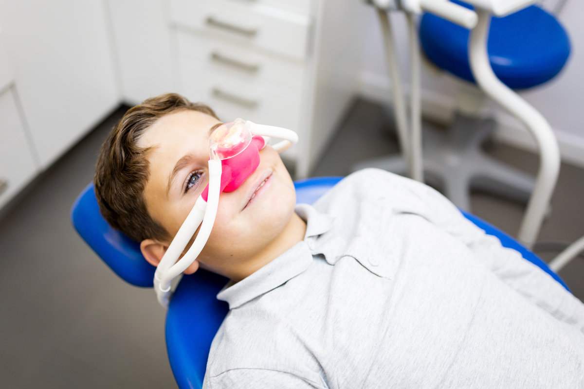 Fear of the dentist! A little boy sits in a dentist's office wearing a nasal mask to breathe nitrous oxide to relax. Concept of feeling relaxed with laughing gas.Fear of the dentist! A little boy sits in a dentist's office wearing a nasal mask to breathe nitrous oxide to relax. Concept of feeling relaxed with laughing gas.