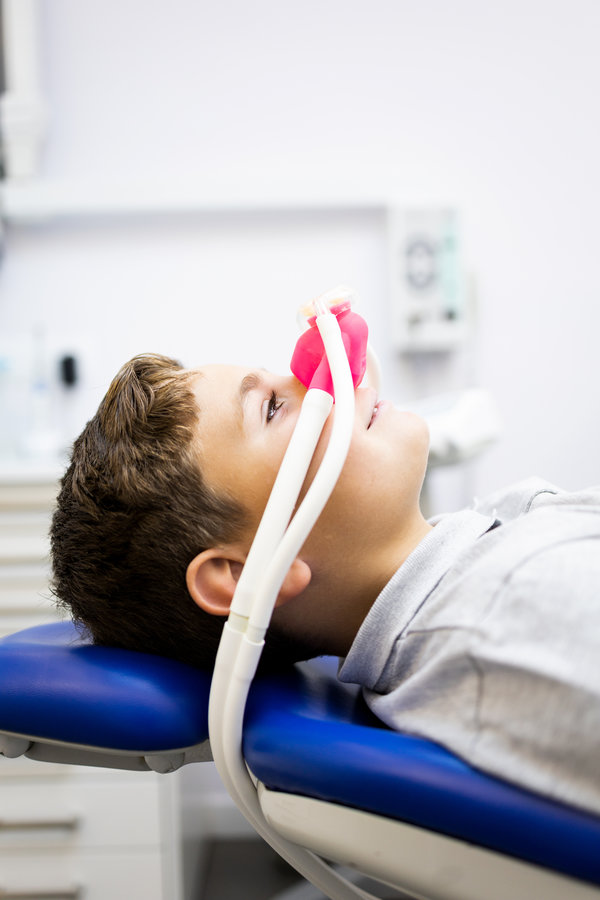Fear of the dentist! Vertical photo of a little boy sits in a dentist's office wearing a nasal mask breathing nitrous oxide to relax. Concept of feeling relaxed with laughing gas. Fear of the dentist! Vertical photo of a little boy sits in a dentist's office wearing a nasal mask breathing nitrous oxide to relax. Concept of feeling relaxed with laughing gas.