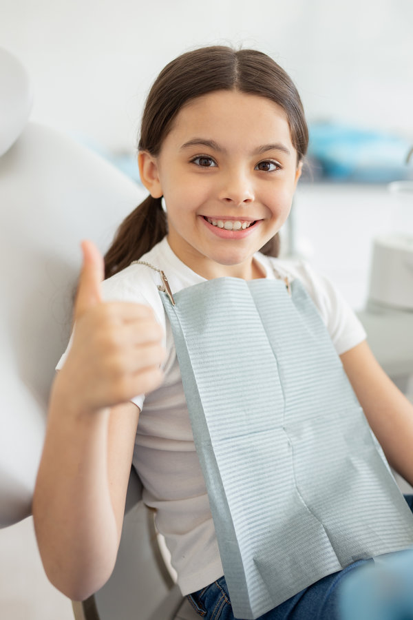 Happy little child sitting in dental chair at dentist office and showing thumb up Happy little child sitting in dental chair at dentist office and showing thumb up